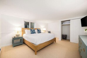Quarto com cama de madeira, luminárias de cabeceira, uma janela e um guarda-roupa.