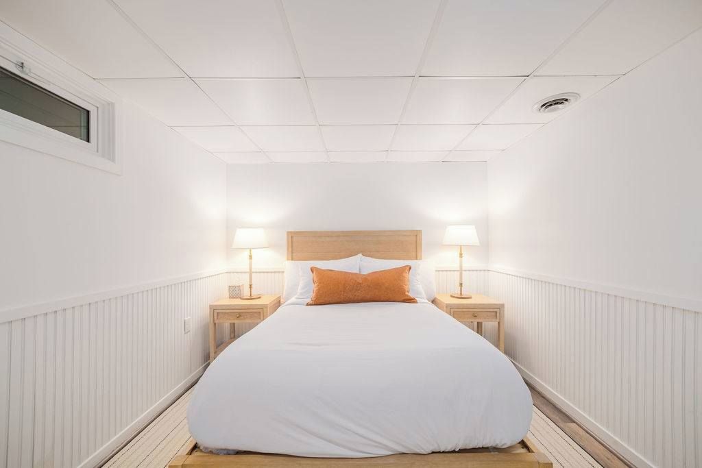 Une chambre d’hôtel étroite, avec un lit simple, deux tables de chevet et une fenêtre.