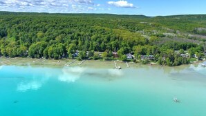 An aerial view of a coastal area with a marina, houses, and dense forest. - Big Glen Lakefront with Hot Tub and Two Fireplaces! (Glen Arbor)