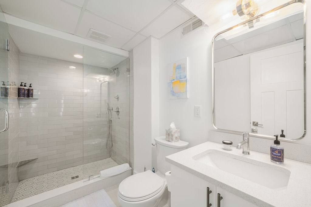 Une salle de bain moderne avec une douche à parois de verre, des toilettes blanches et un lavabo surmonté d’un miroir.