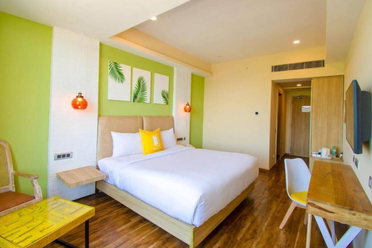 Una habitación de hotel con cama, mesita de noche de madera, silla, escritorio y televisor.