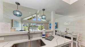 A modern kitchen with a large island, stainless steel sink, and pendant lighting. - Coconuts101-BEACH FRONT COMPLEX-1BR ground level-ByIslandRealEstate (Holmes Beach)
