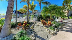 A tropical resort with palm trees, a pool, and a well-maintained garden area. - Coconuts101-BEACH FRONT COMPLEX-1BR ground level-ByIslandRealEstate (Holmes Beach)