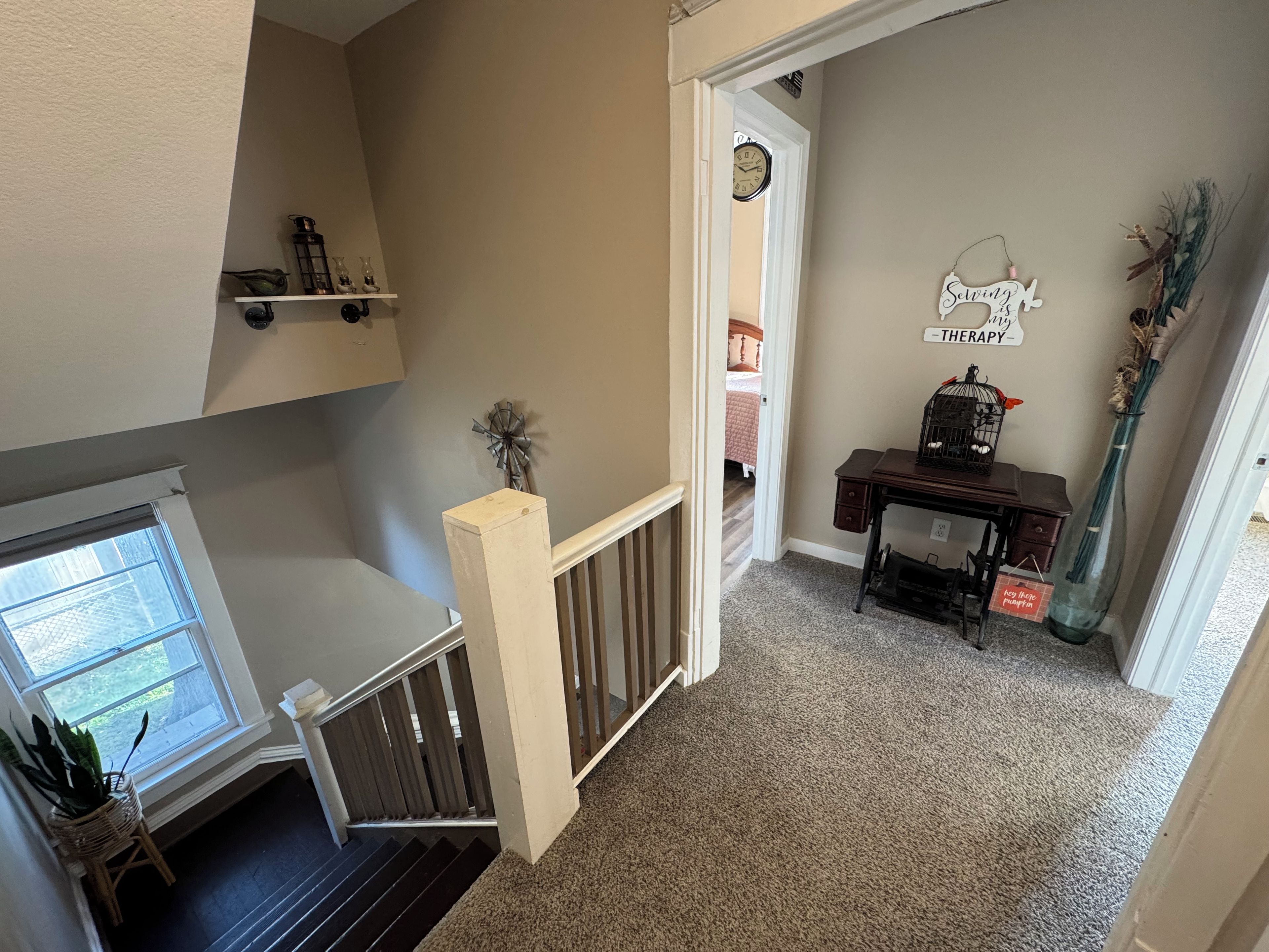 A hallway with a staircase, a decorative wall clock, a small table with a birdcage, and a sign that reads 'Healing Therapy.'