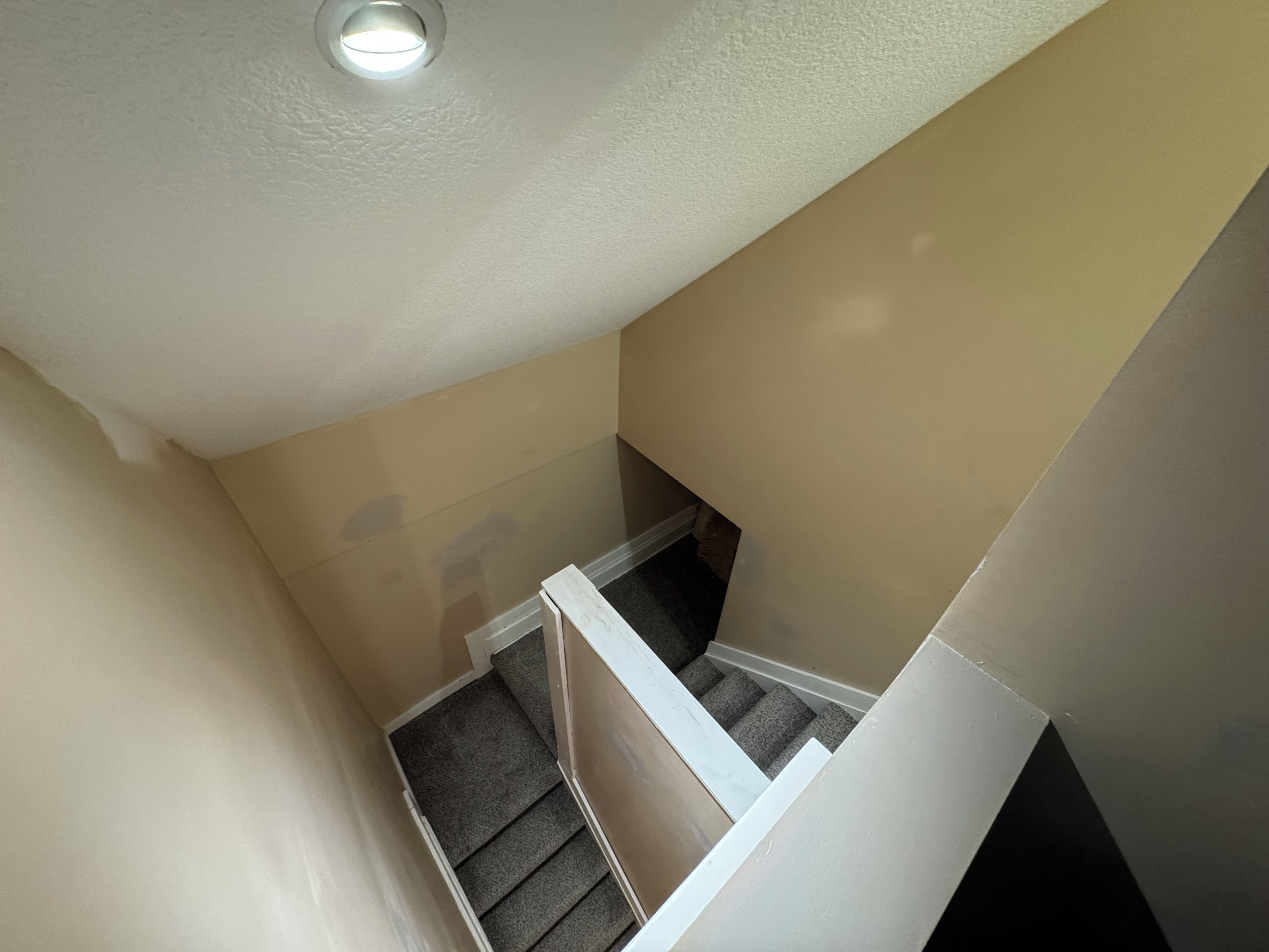 A corner of a room with a white ceiling, a beige wall, and a white baseboard.