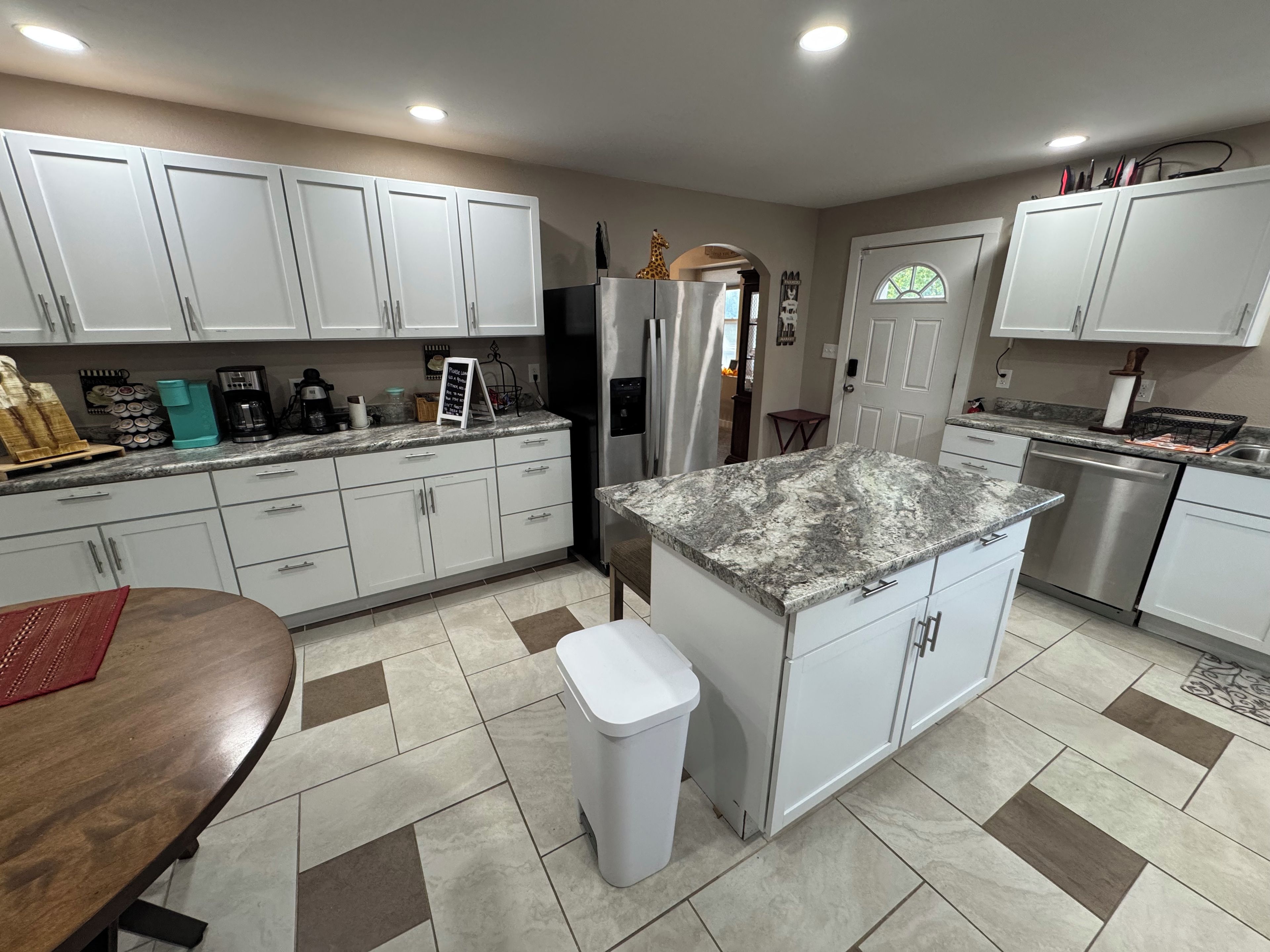 A modern kitchen with white cabinets, a granite countertop, stainless steel appliances, and a tiled floor.
