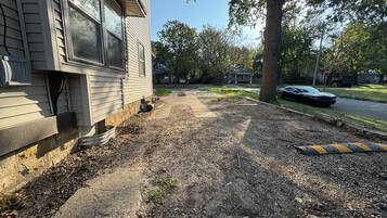 A residential driveway with a house on the left, a tree on the right, and a parked car.