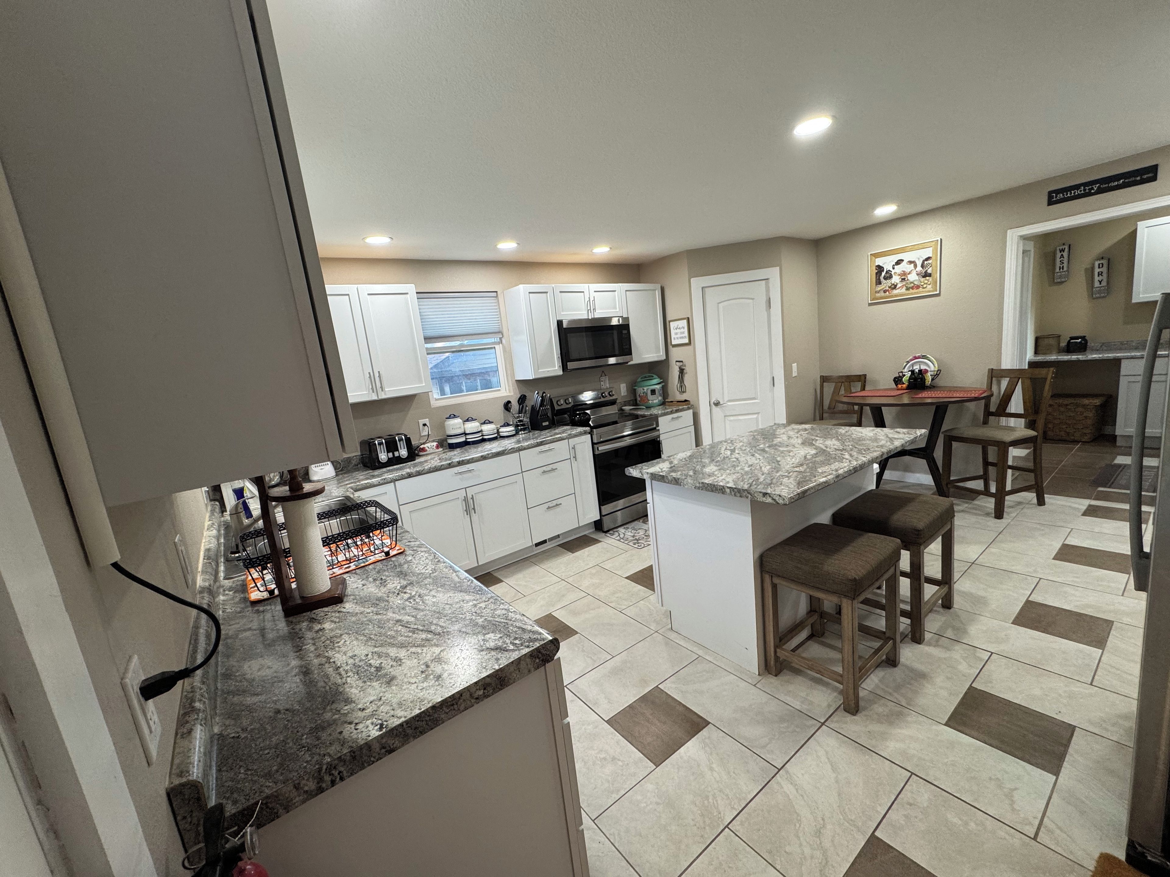 A modern kitchen with white cabinets, a granite countertop, and a dining area with wooden chairs.