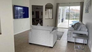 A spacious living room with a grey sofa, a smaller grey sofa, and a coffee table. There is a flat-screen TV mounted on the wall, and a large window with curtains. - Retreat at Genoa  (Port St. Lucie)