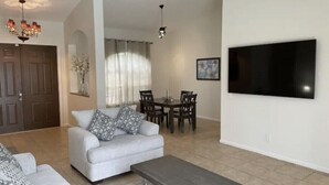 A living room with a sofa, coffee table, dining table, chairs, and a flat-screen TV mounted on the wall. - Retreat at Genoa  (Port St. Lucie)