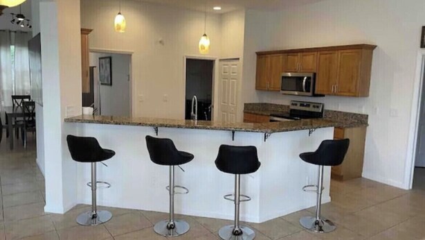 A modern kitchen with a central island, bar stools, wooden cabinets, and a microwave. - Retreat at Genoa  (Port St. Lucie)
