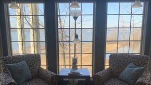A room with two patterned armchairs facing a window with a view of trees and water. There is a small table with a decorative item in the center. - Lake Front Cottage with private sandy beach (Cadiz)