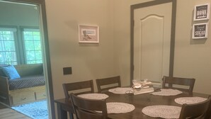 A dining area with a wooden table and chairs, a framed picture on the wall, and a sign above the door. - Lake Front Cottage with private sandy beach (Cadiz)