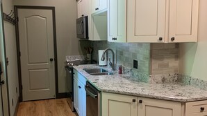 A kitchen with white cabinets, a granite countertop, and a stainless steel sink. - Lake Front Cottage with private sandy beach (Cadiz)