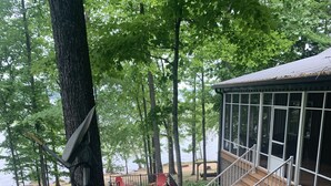 A covered deck with a wooden staircase leading to a building with large windows. - Lake Front Cottage with private sandy beach (Cadiz)