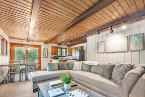 Et moderne interiør med træloft, en stor L-formet sofa, et spiseområde og et køkken.
