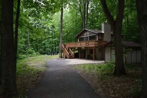 A cabin with a porch and a staircase leading to a deck, surrounded by dense forest.