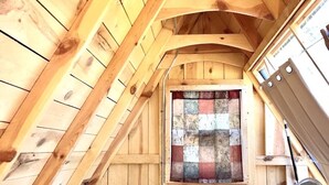 Un dormitorio estilo ático con techo inclinado, ventana acolchada, cama y un ventilador de pie.