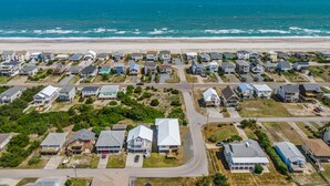 Vue aérienne d’une zone résidentielle côtière, avec des maisons, des routes et une plage.
