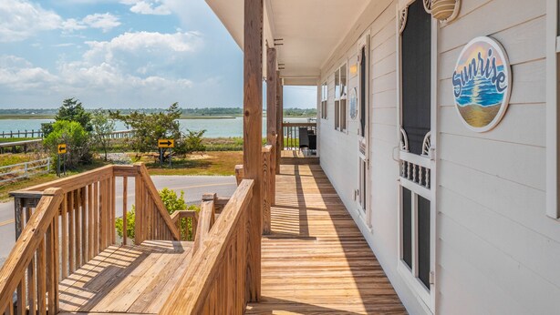 Une terrasse en bois offrant une vue sur l’eau, un panneau indiquant une direction et un bâtiment portant l’inscription « Sunrise ».