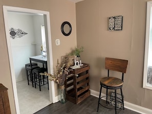 A room with a wooden chair, a small table with decorative items, a mirror, and a wall with a motivational quote.