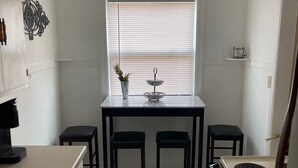 A compact kitchen with a dining area, a stove, and a window with blinds.