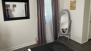 A bedroom with a bed, a mirror, a window with curtains, and a door.