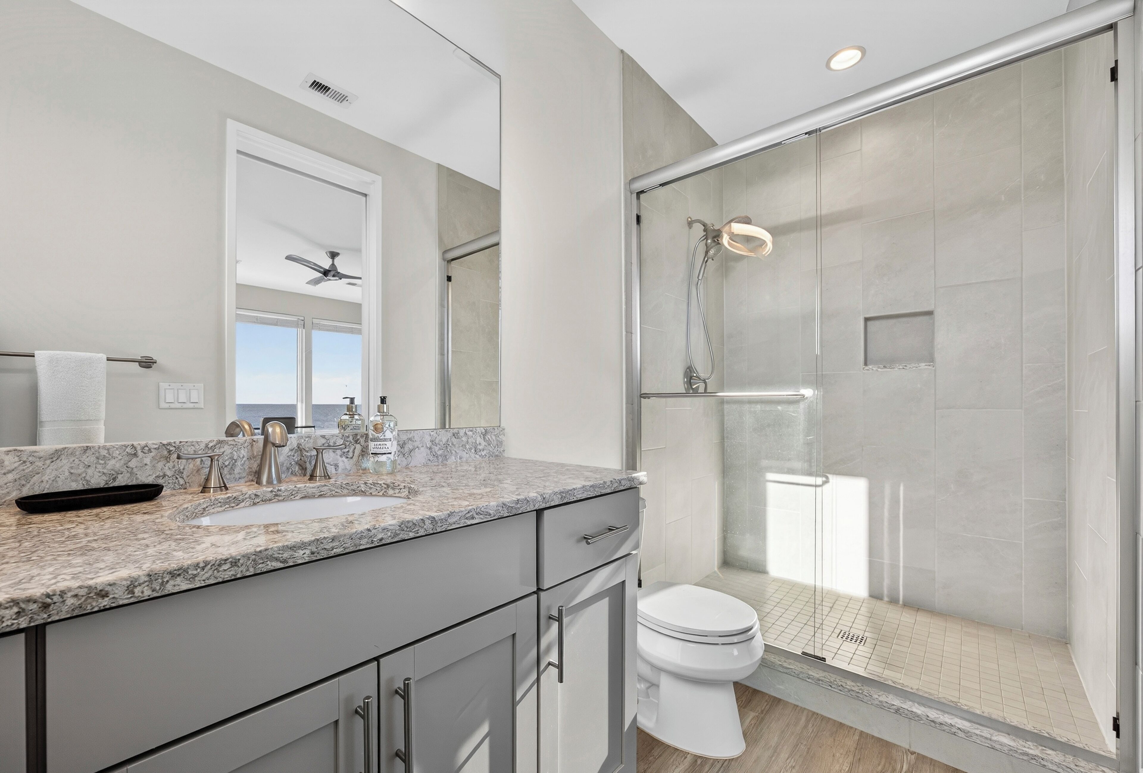 A modern bathroom with a glass shower enclosure, a large mirror, and a marble countertop.