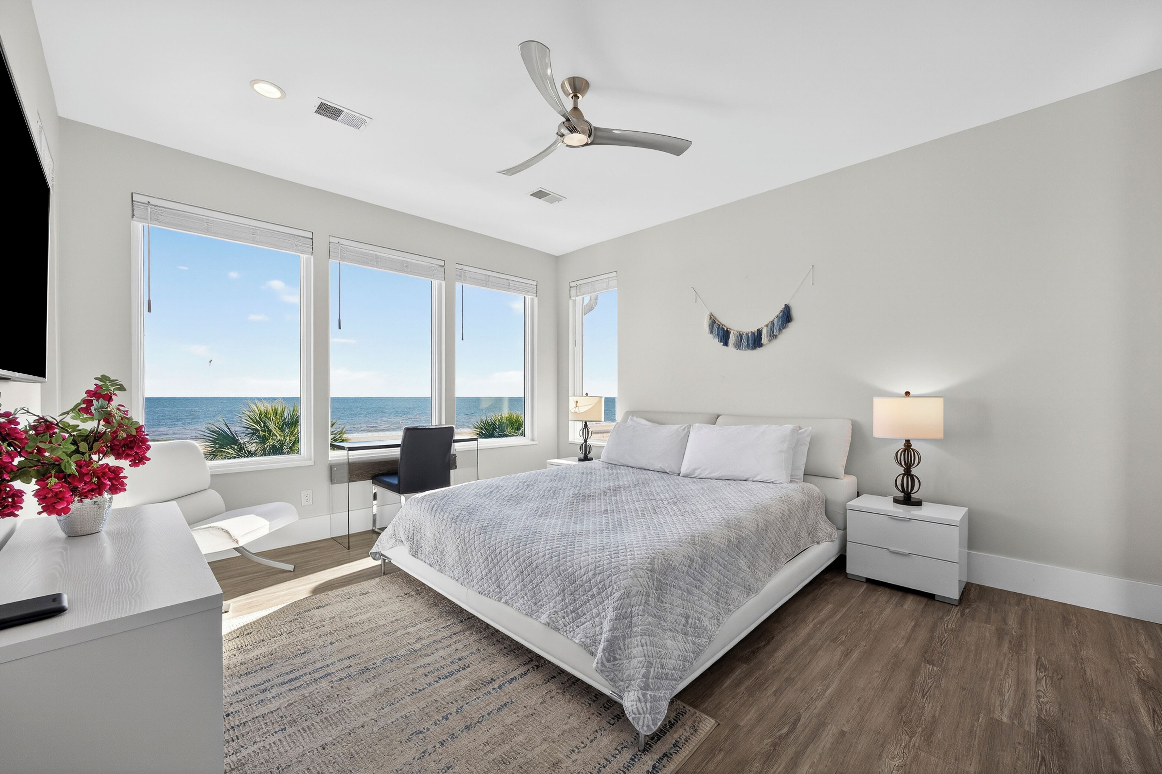 A modern bedroom with a large bed, a desk, and a view of the ocean.