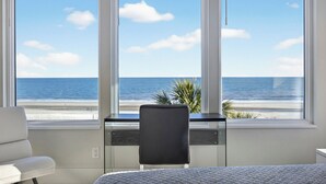 A room with a large window overlooking a beach, a desk, and a chair. - Newly Built 7-bedroom Oceanfront Stunner with private pool. (Hilton Head Island)