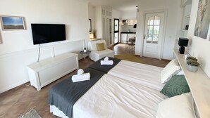 Ett hotellrum med en stor säng, en TV, ett skrivbord och ett litet kök.