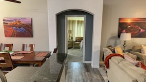 A dining area with a wooden table and chairs, a kitchen area with a countertop, and a living room with a sofa and a lamp. - Pool & EV Charger @ Family Friendly comfy house in the heart of Queen Creek (Queen Creek)