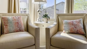 A room with two leather armchairs, a white side table with a lamp, and a view of the outdoors through large windows. - Pool & EV Charger @ Family Friendly comfy house in the heart of Queen Creek (Queen Creek)