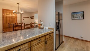 A kitchen with granite countertops, wooden cabinetry, a stainless steel refrigerator, and a dining area with wooden chairs and a table. - Updated Condo Near Mountain, Free Shuttle, Pool, Hot Tub! (Steamboat Springs)