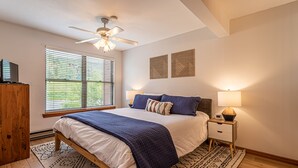 A bedroom with a bed, bedside tables, a ceiling fan, and a window with blinds. - Updated Condo Near Mountain, Free Shuttle, Pool, Hot Tub! (Steamboat Springs)