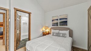 A bedroom with a bed, a nightstand with a lamp, and a door leading to another room. - Renovated 3-Bedroom Condo at Timber Run – Spacious Mountain Retreat with Prime L (Steamboat Springs)