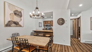 A dining area with a wooden table and chairs, a chandelier, and a kitchen in the background. - Renovated 3-Bedroom Condo at Timber Run – Spacious Mountain Retreat with Prime L (Steamboat Springs)