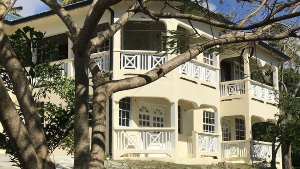 A two-story building with balconies, large windows, and a grassy lawn. - Beautiful, tranquil Home. 8 minutes from the International Airport (Vieux Fort)