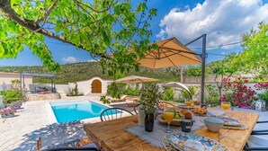 A poolside dining area with a table set for breakfast, surrounded by greenery and a view of a pool and hills. - Villa Little Paradise with a private pool, 4 bedrooms, 2 living areas, 3km from the beach in Marina (Marina)