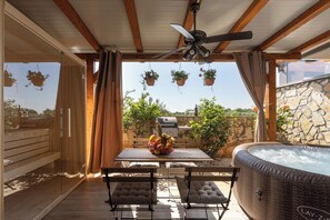 An outdoor patio with a hot tub, wooden furniture, hanging planters, and a stone wall. - Apartment Apartman Lucia (Istria - Novigrad) (Novigrad)