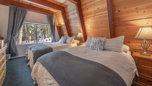 A cozy log cabin bedroom with two beds, a dresser, and a window with curtains.