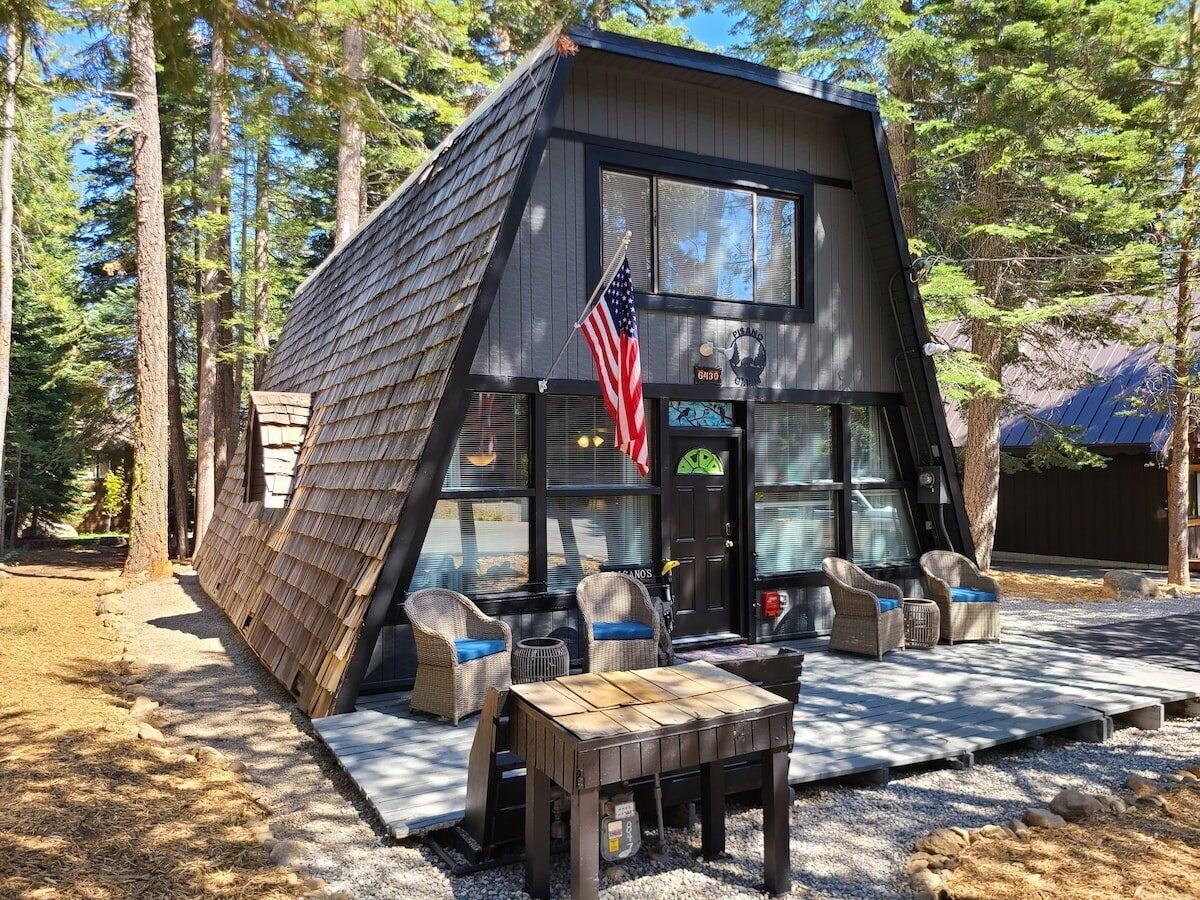 A cabin with a sloped roof, a porch with wicker furniture, and an American flag.