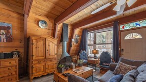 A cozy cabin interior with wooden walls, a fireplace, a sofa, and a dining area.