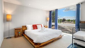 A bedroom with a large bed, a nightstand, a lamp, and a view of a balcony.