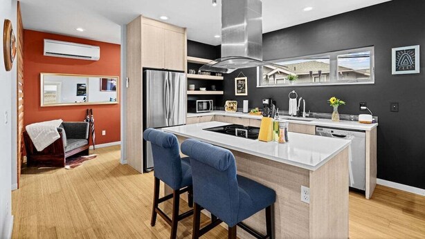 A modern kitchen with a central island, bar stools, and a large window.