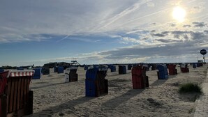 Une plage bordée de rangées de cabanes de plage numérotées, sous un ciel dégagé où le soleil brille.