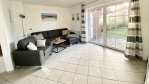 Un salon moderne avec un canapé noir, une table basse et une vue sur un jardin, visible à travers une porte-fenêtre coulissante.