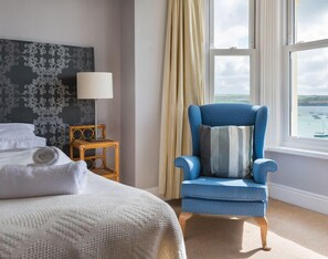 A hotel room with a bed, a chair, a nightstand, a lamp, and a window with a view of the sea. - 4 The Terrace (Wadebridge)