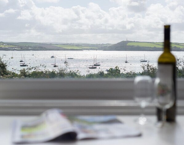 A view of a lake with sailboats, a bottle of wine, and a window sill with a book.
