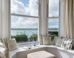A bay window with a view of boats on the water, a bottle of wine, and a magazine on the windowsill.